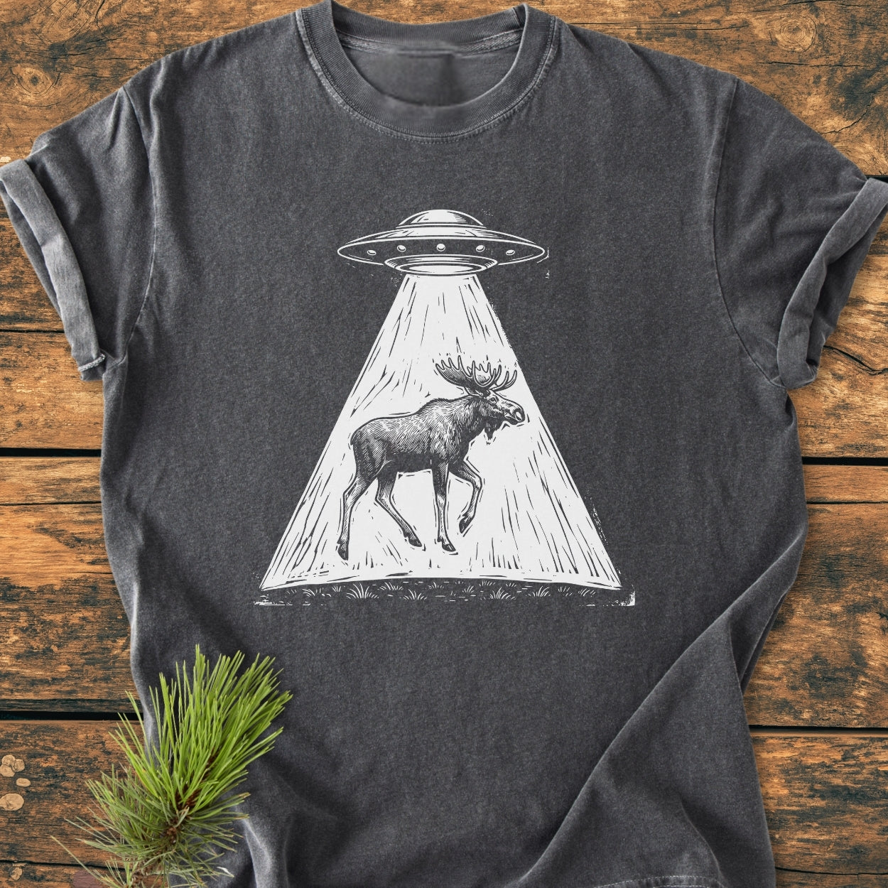 The Only Way Is Up - Vintage Wash Tee: Charcoal-gray T-shirt featuring a white line-art of a UFO beaming up a moose, laid on rustic wood with a pine sprig accent.