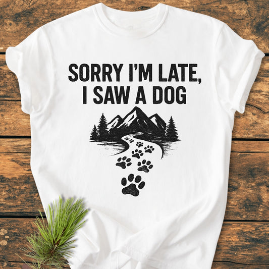 Sorry I'm Late - Vintage Wash Tee features bold text and a nature graphic with paw prints, laid on wood, styled with a pine sprig, showcasing its relaxed fit and cozy, soft-washed fabric.