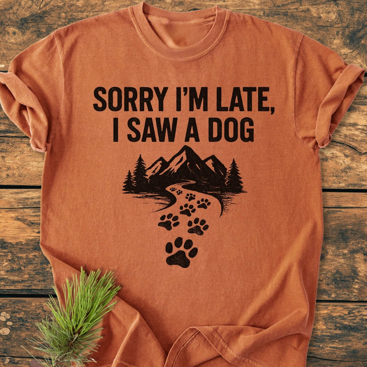 Sorry I'm Late - Vintage Wash Tee featuring bold text and mountain silhouette with paw prints, laid on wood. Made from soft, pre-shrunk 100% ring-spun cotton for comfort and durability.