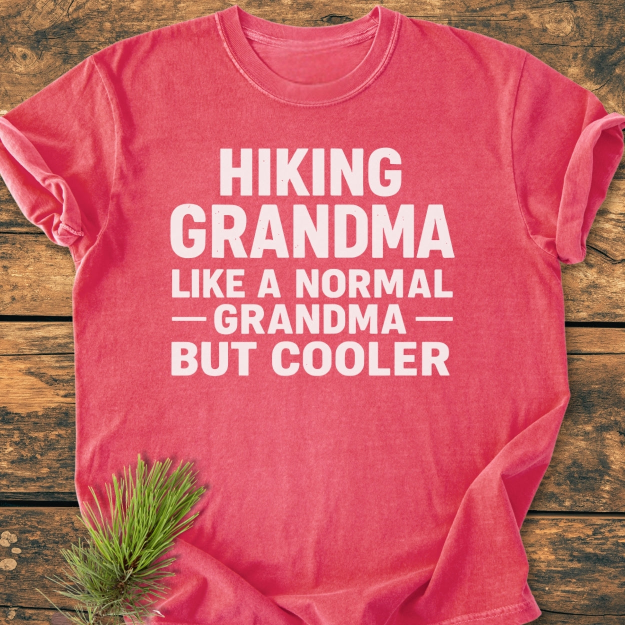 Heather-red Hiking Grandma - Vintage Wash Tee with bold white lettering, laid flat. Pine sprig accent on wooden surface. Soft, relaxed fit, 100% ring-spun cotton, double-stitched, durable.