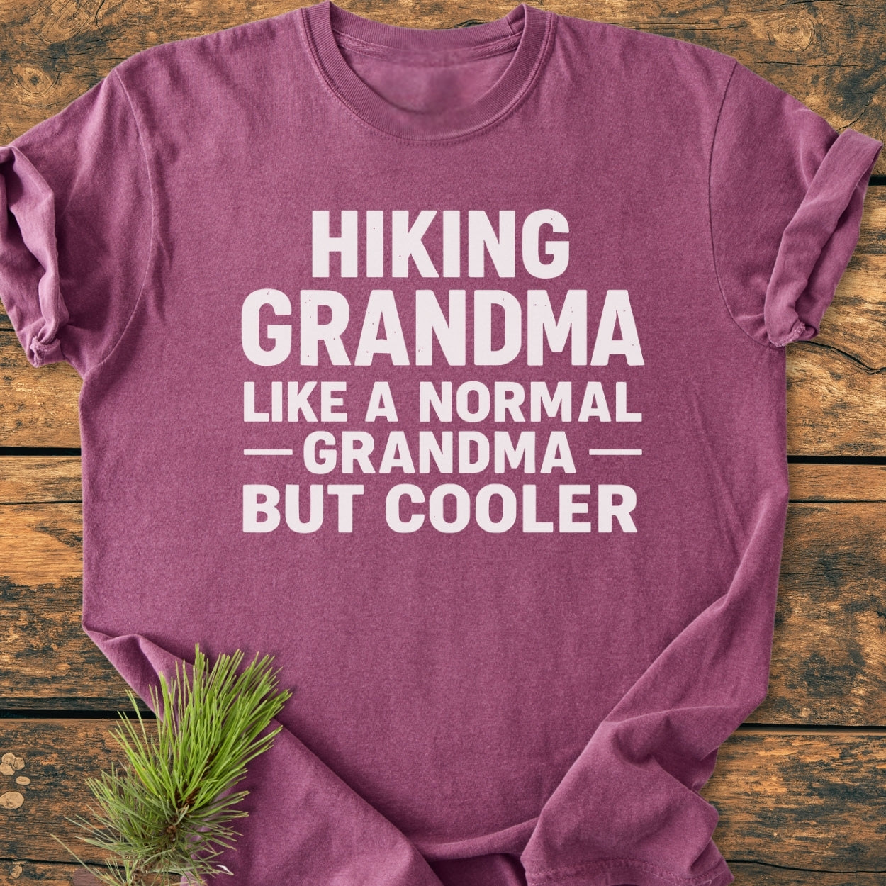 Heather-purple Hiking Grandma - Vintage Wash Tee with bold white slogan, laid flat on wood background, featuring a pine sprig. Made of soft, durable, pre-shrunk 100% ring-spun cotton in relaxed fit.