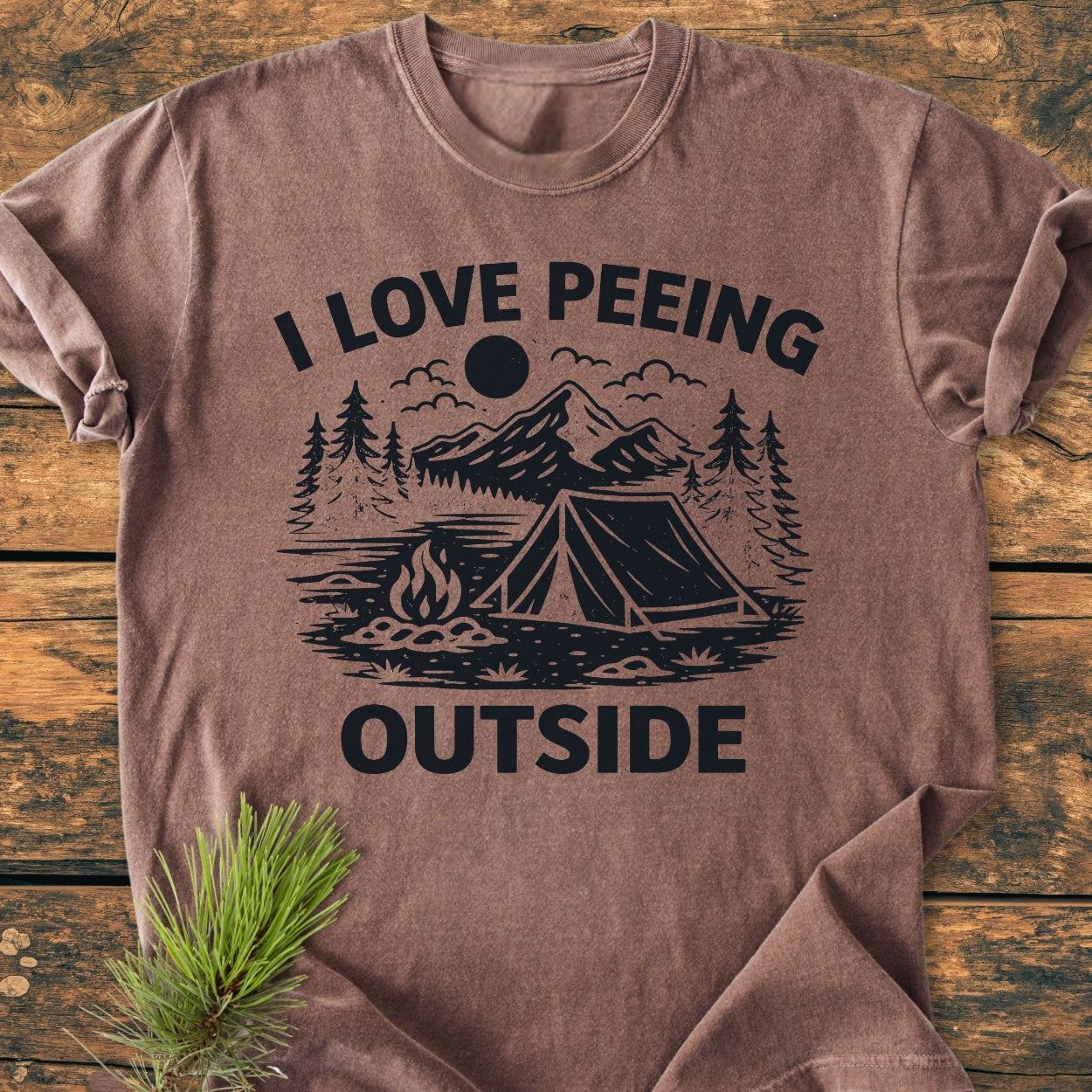 I Love Peeing Outside - Vintage Wash Tee features a stylized outdoor scene with pine trees, mountains, tent, and campfire. Laid flat, showcasing its durable, relaxed fit and soft-washed cotton fabric.