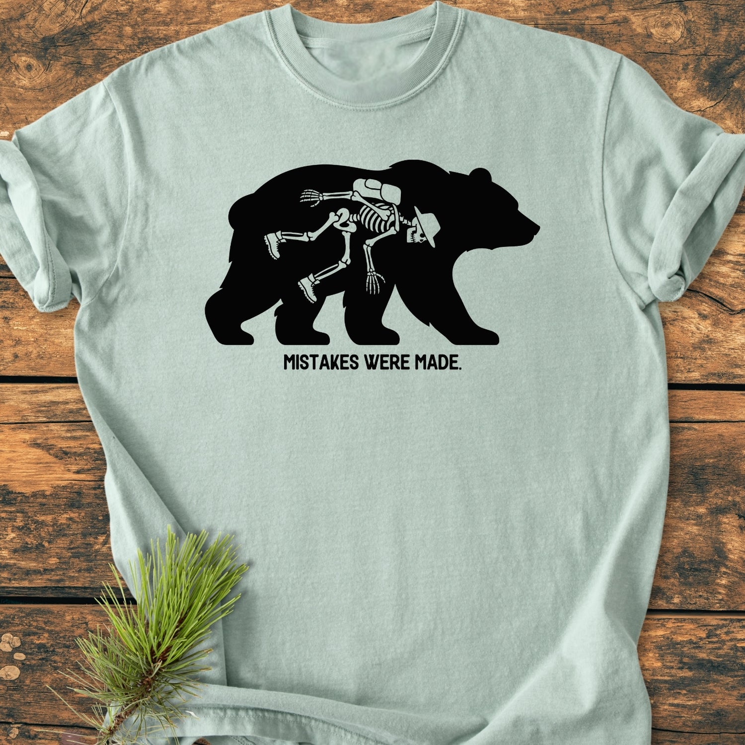 Mistakes Were Made - Vintage Wash Tee features a mint T-shirt with a black bear silhouette, revealing a white-line hiker skeleton inside, and the phrase MISTAKES WERE MADE beneath in bold letters.
