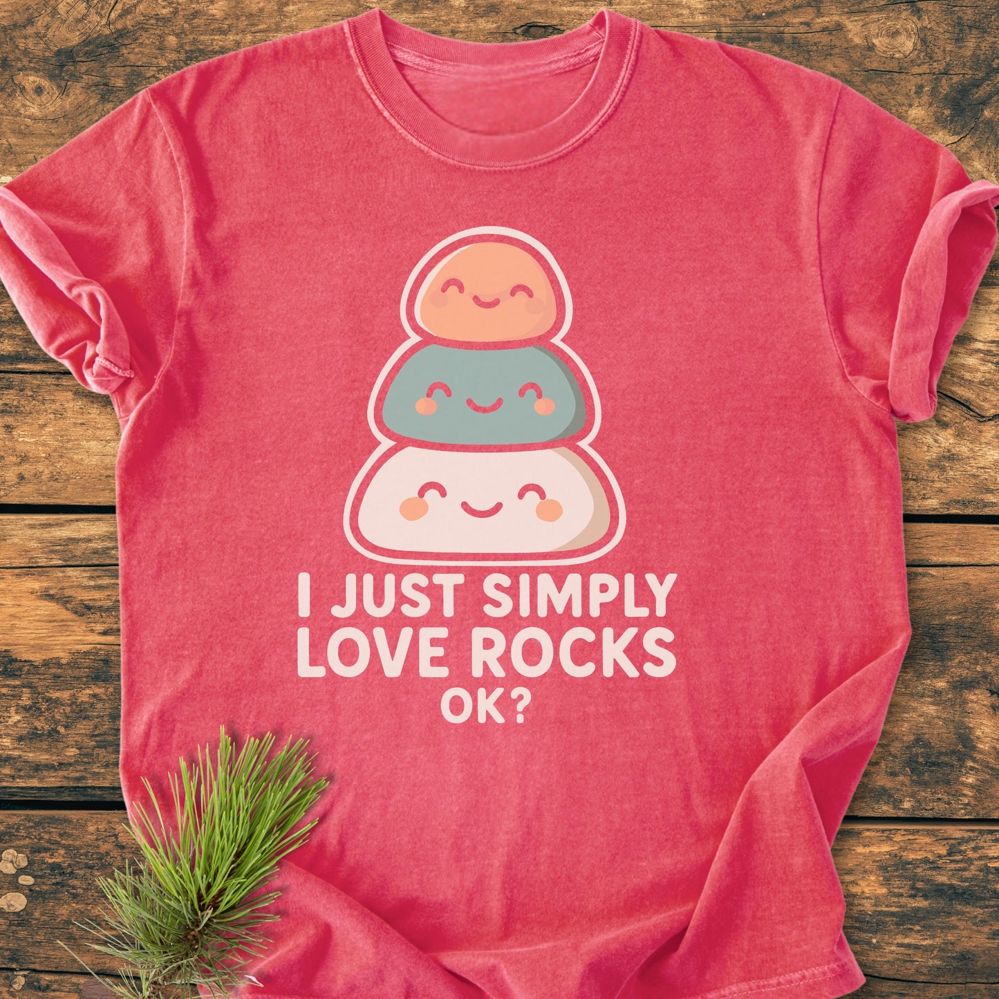 Heathered red I Just Simply Love Rocks OK? - Vintage Wash Tee featuring cheerful stacked rock graphics and playful text, laid flat on wood with pine sprig accentuating its cozy, relaxed charm.