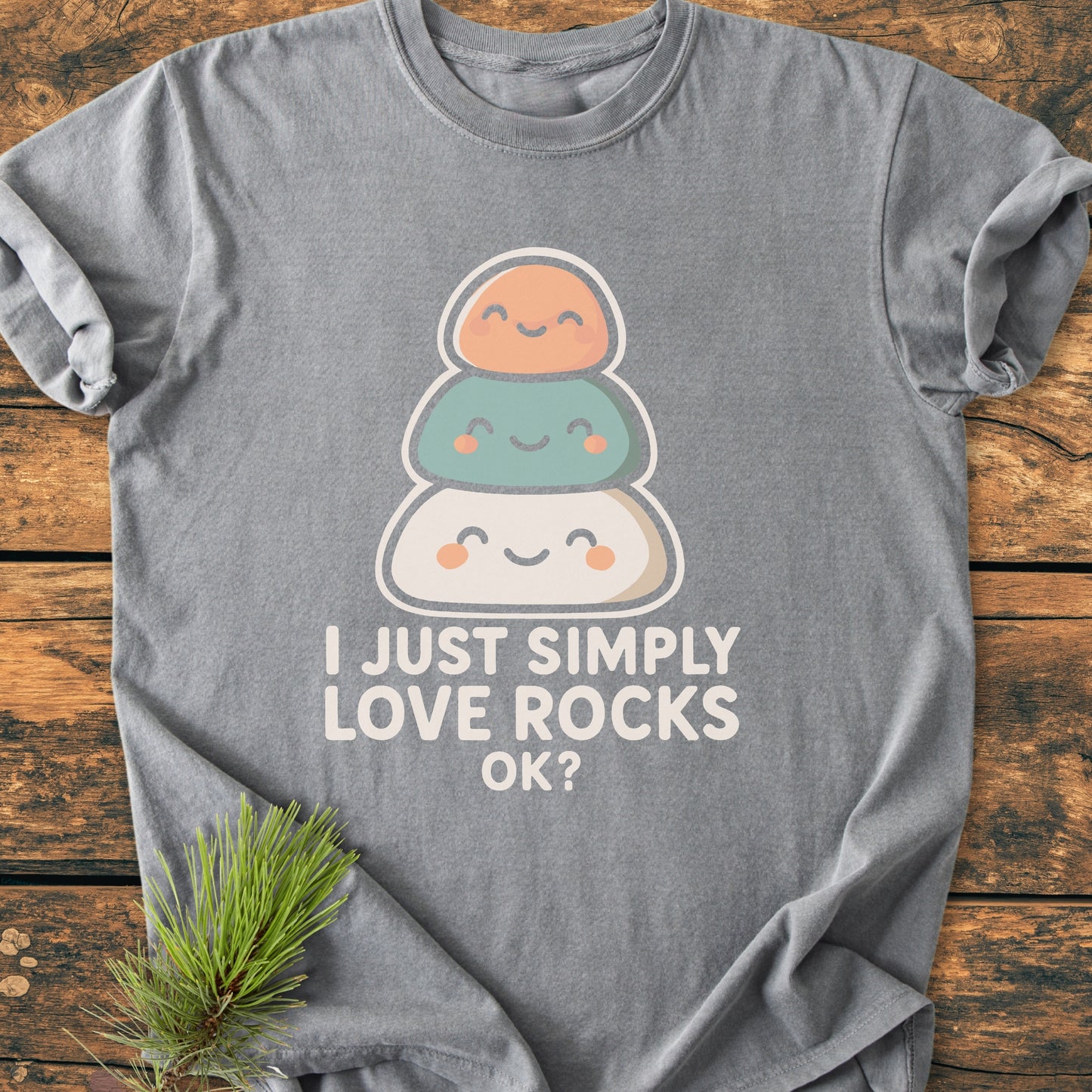 Heather-gray I Just Simply Love Rocks OK? tee with cartoon rocks graphic, laid flat on wood. Features soft-washed, durable Comfort Colors fabric, relaxed fit, pre-shrunk ring-spun cotton.