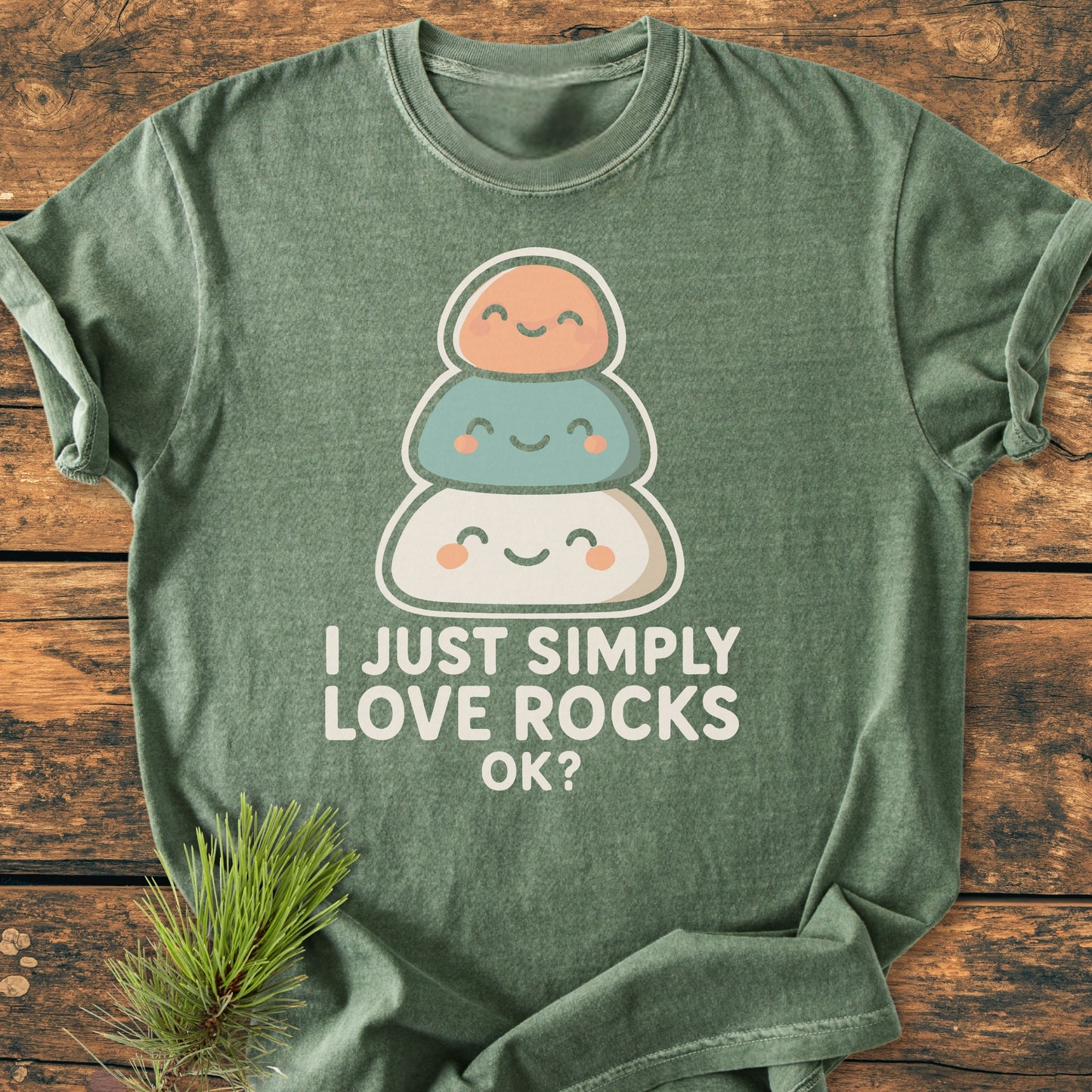 Heather-green I Just Simply Love Rocks OK? vintage wash tee with smiling stone stack design, styled on wood with pine sprig. Soft, relaxed fit, 100% ring-spun cotton.