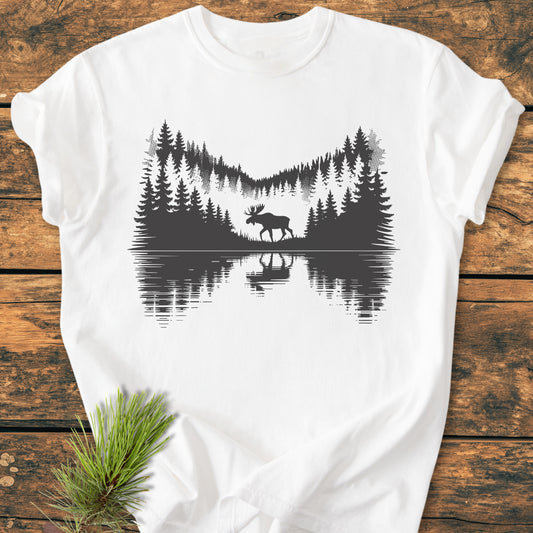 Lone Wanderer - Vintage Wash Tee displays a moose and forest silhouette on a soft, white backdrop, laid on rustic wood. Comfortable and durable, made from 100% ring-spun cotton for daily wear.