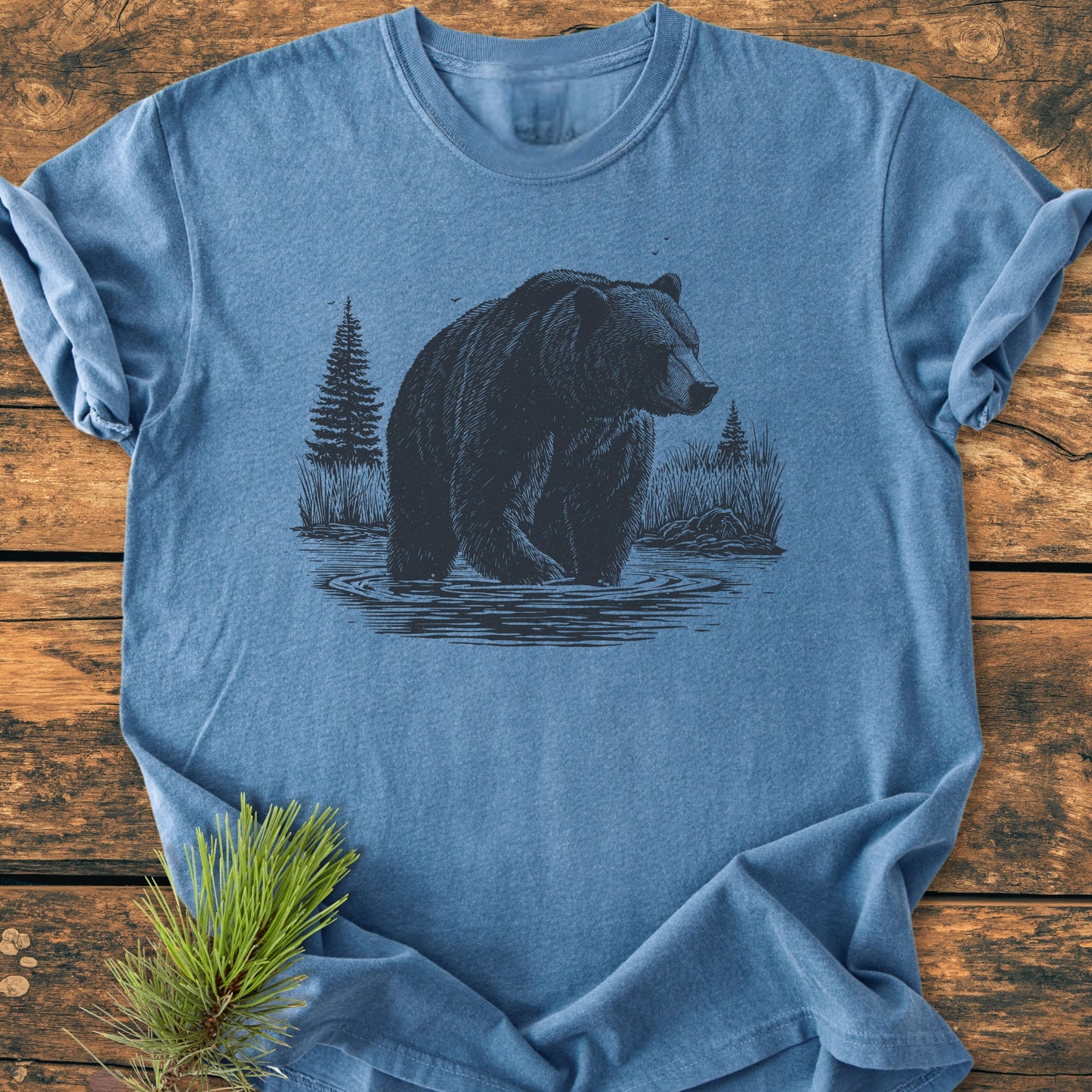 Majestic Grizzly - Vintage Wash Tee featuring a bear line-drawing and pine scenery, laid on wood. Crafted by Comfort Colors, this pre-shrunk, relaxed-fit, 100% cotton tee ensures comfort and durability.