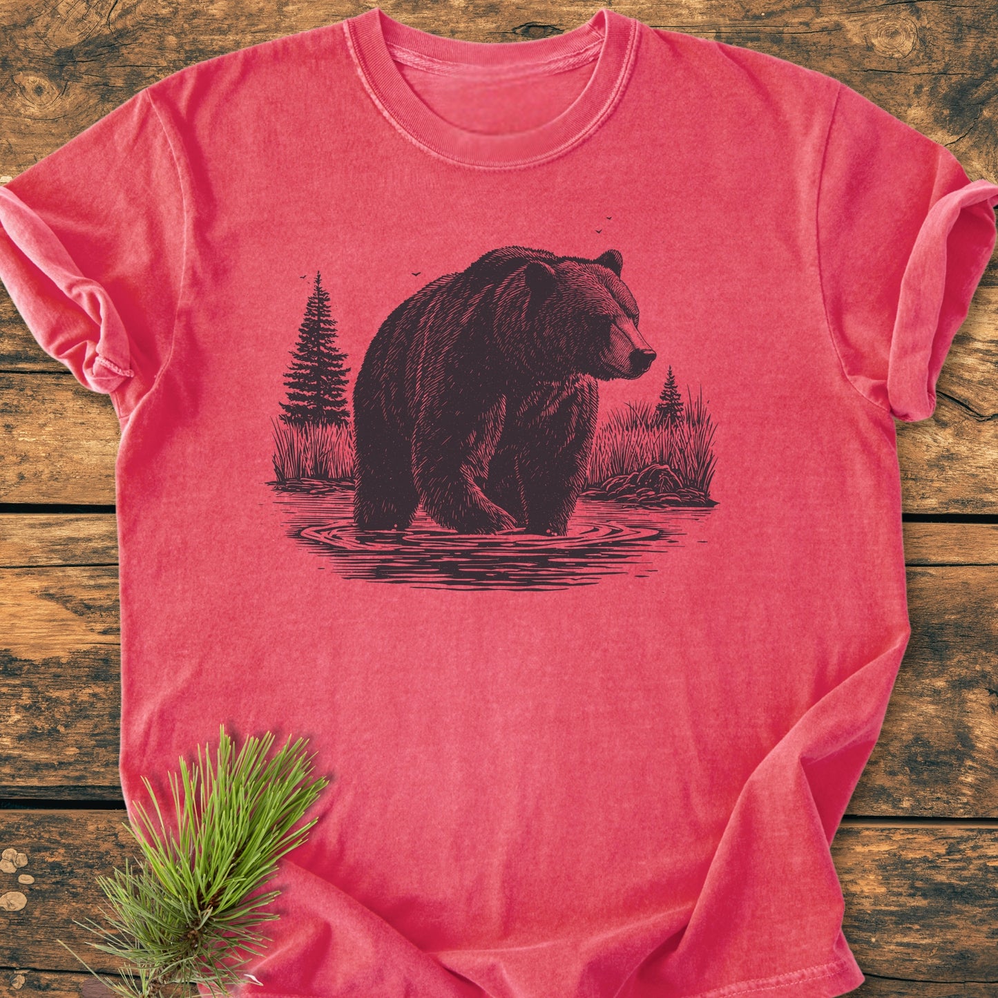 Majestic Grizzly - Vintage Wash Tee featuring a detailed bear illustration, laid flat on wood, with pine branch accentuating the outdoorsy theme; crafted from soft, durable, 100% ring-spun cotton.