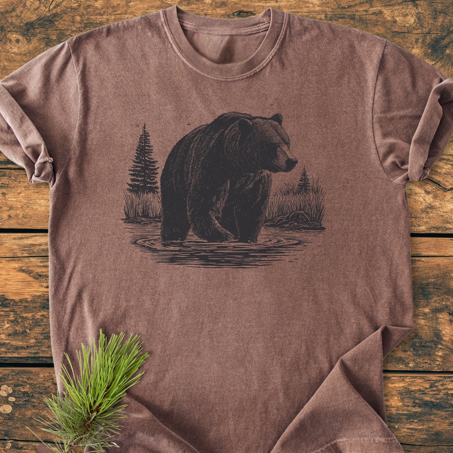 Majestic Grizzly - Vintage Wash Tee laid flat, features a bear graphic in water with pine trees and grasses. Soft, garment-dyed, ring-spun cotton ensures comfort and durability.