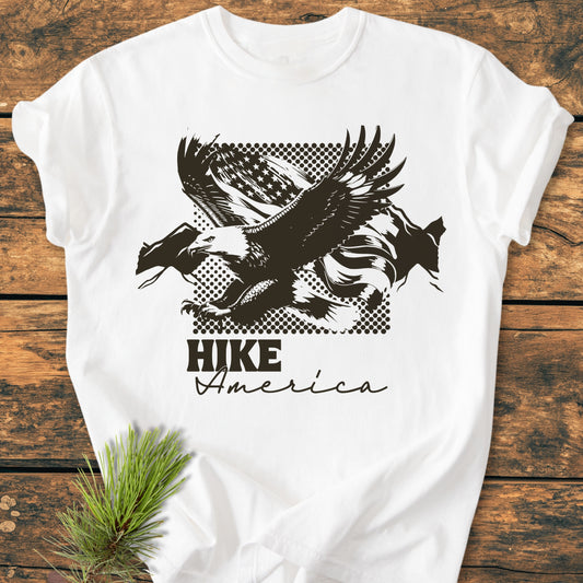 Hike America - Vintage Wash Tee: White T-shirt with a bold graphic of a bald eagle and flag, laid on wood. Features include garment-dyed, soft-washed cotton for comfort and durability.