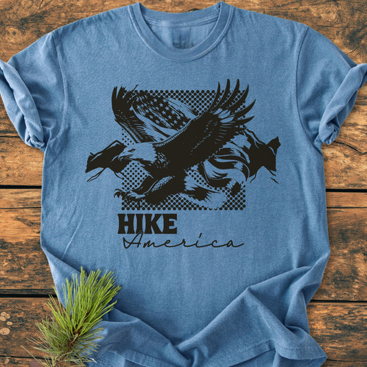 Hike America - Vintage Wash Tee features a black bald eagle graphic over a waving American flag, printed on a light-blue shirt, showcasing its relaxed fit and cozy garment-dyed fabric.