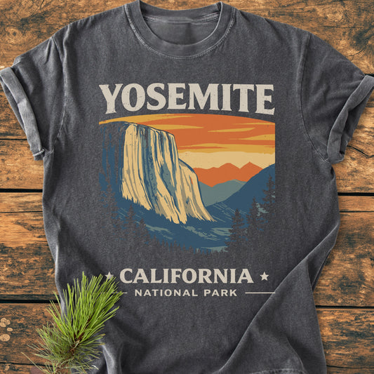 Yosemite National Park - Vintage Wash Tee featuring distressed white YOSEMITE text and El Capitan illustration, laid on wood with pine sprig. Soft, garment-dyed cotton ensures comfort and durability.
