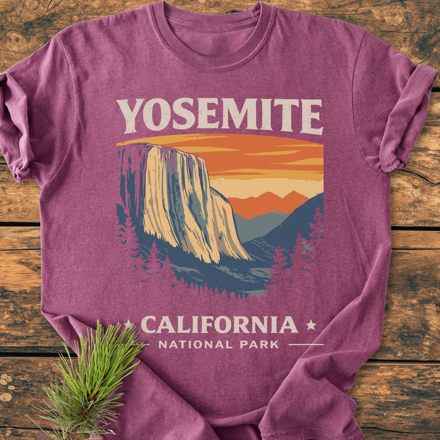 Yosemite National Park - Vintage Wash Tee features a vintage El Capitan design with pine trees, under an orange sunset sky, displayed on a rustic surface. Made from soft, durable, ring-spun cotton.