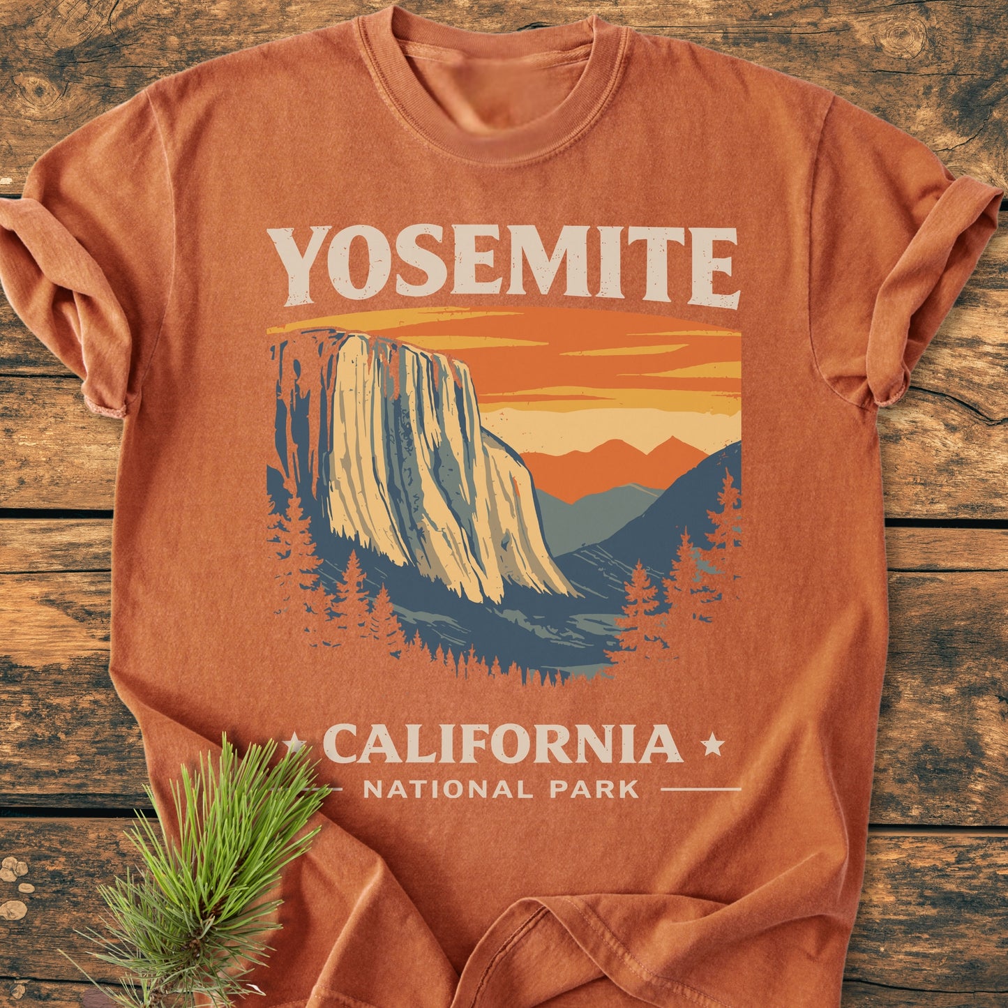 Yosemite National Park - Vintage Wash Tee features an El Capitan graphic with a sunset backdrop. The relaxed fit, 100% cotton shirt is displayed on wood, showcasing its rustic charm.