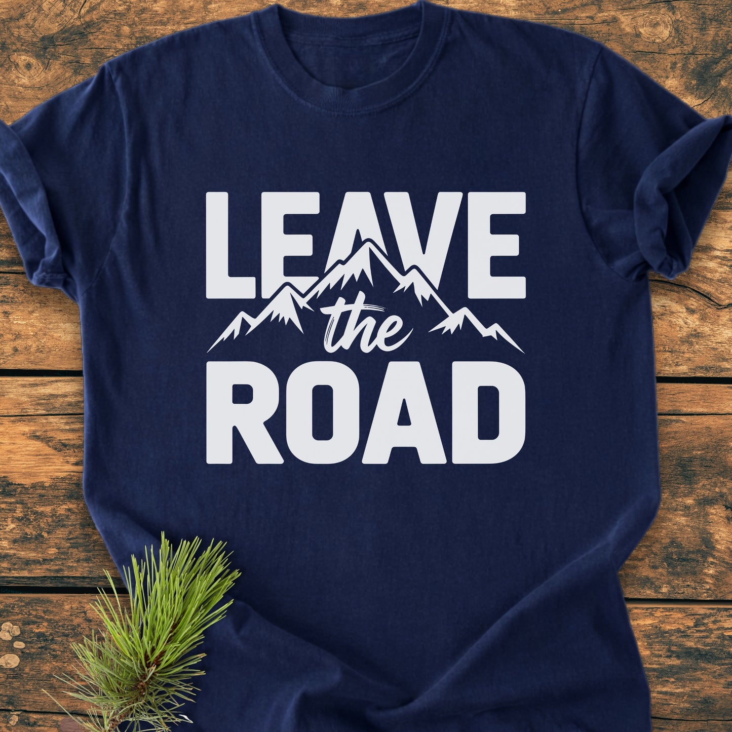 Leave The Road - Vintage Wash Tee in navy, featuring white mountain-themed text, laid on wood with a pine sprig. Made from soft, durable, pre-shrunk 100% ring-spun cotton with a relaxed fit.