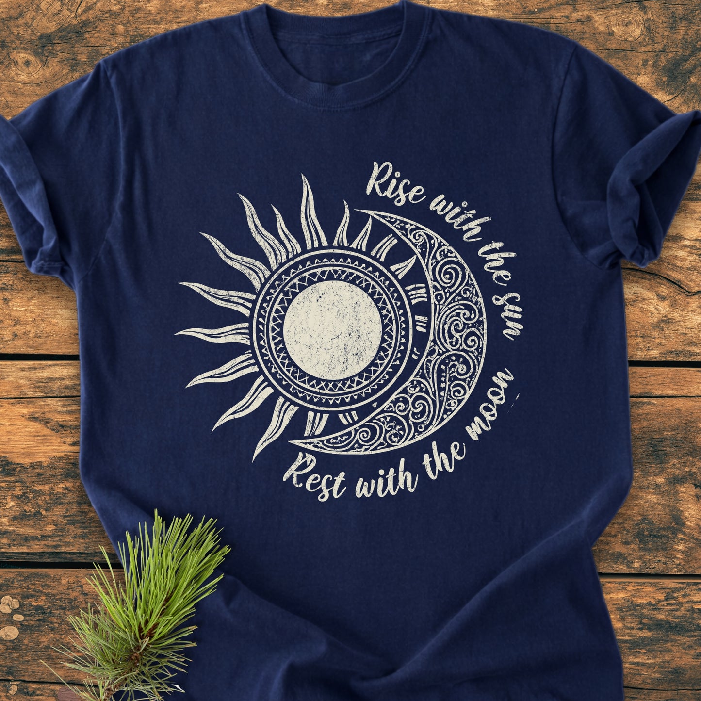 Navy-blue Sun & Moon Mystical Boho - Vintage Wash Tee with a sun and crescent moon design, laid on wooden surface with pine sprig; text reads Rise with the sun Rest with the moon.