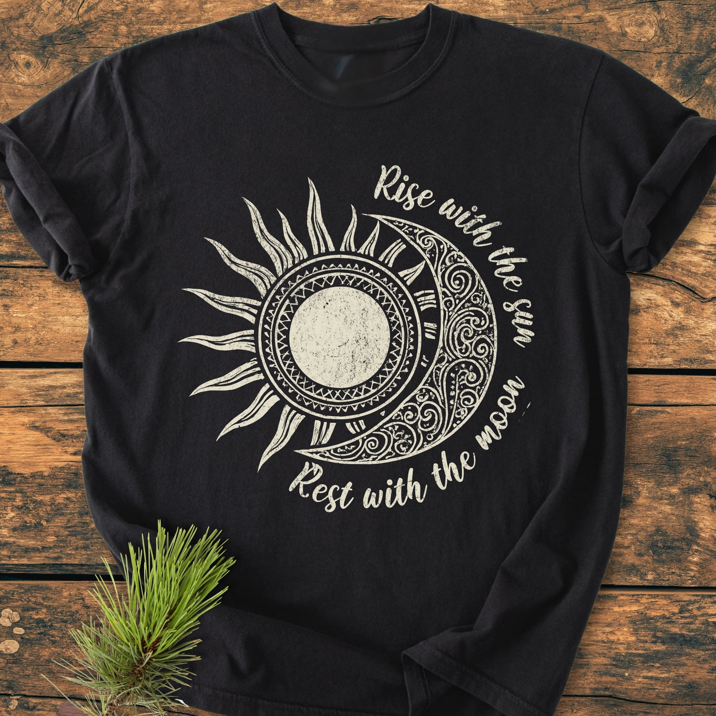 Sun & Moon Mystical Boho - Vintage Wash Tee featuring a sun-and-moon design with Rise with the sun, Rest with the moon text, laid flat on a wooden surface with a pine sprig.