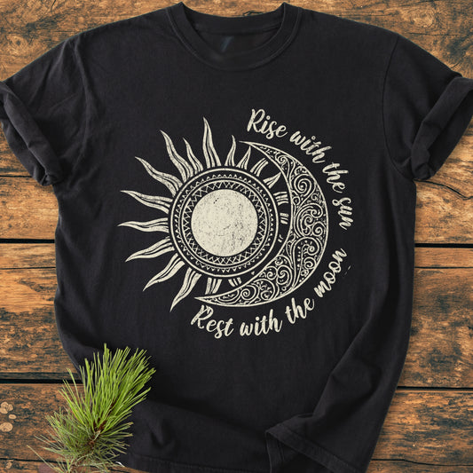 Sun & Moon Mystical Boho - Vintage Wash Tee featuring a sun-and-moon design with Rise with the sun, Rest with the moon text, laid flat on a wooden surface with a pine sprig.
