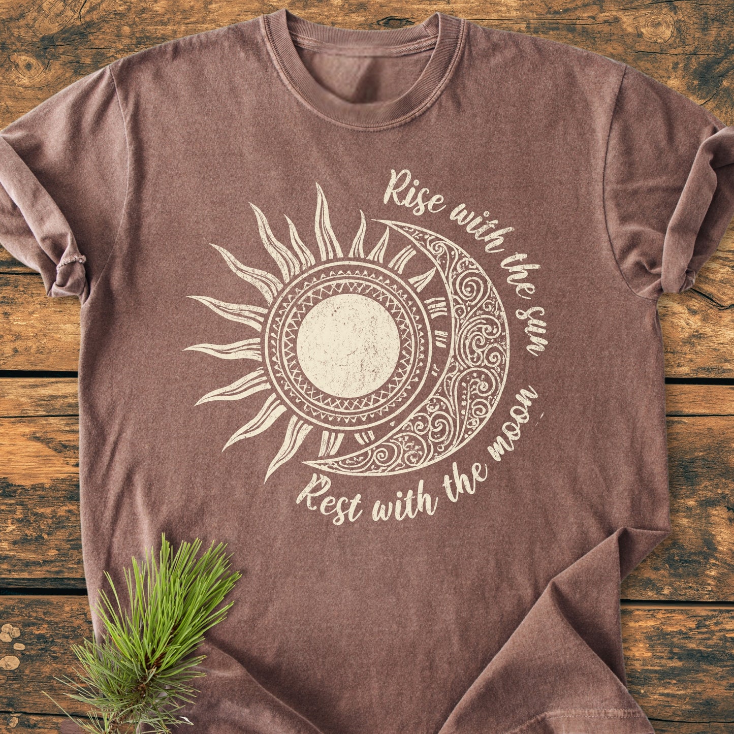 Sun & Moon Mystical Boho - Vintage Wash Tee features a stylized sun/moon graphic with Rise with the sun, Rest with the moon text, displayed on a rustic wooden surface with pine sprig accent.