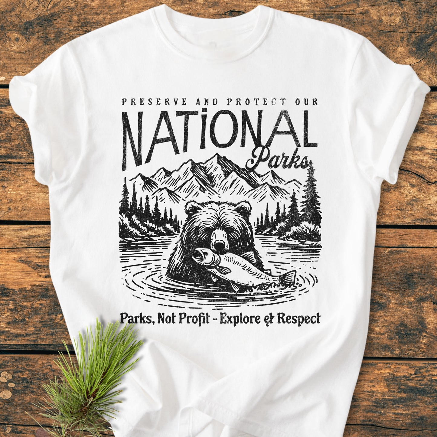 Preserve Our National Parks - Vintage Wash Tee features a bear with fish, pine trees, and mountains. Black ink print on a white, soft-washed, relaxed fit, 100% ring-spun cotton T-shirt.