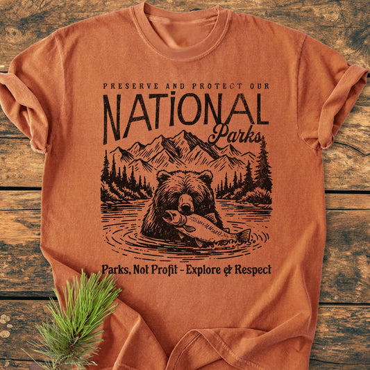 Preserve Our National Parks - Vintage Wash Tee features a rust-orange hue, with a nature graphic of mountains, pine trees, and a bear, advocating conservation on a soft, relaxed-fit cotton shirt.