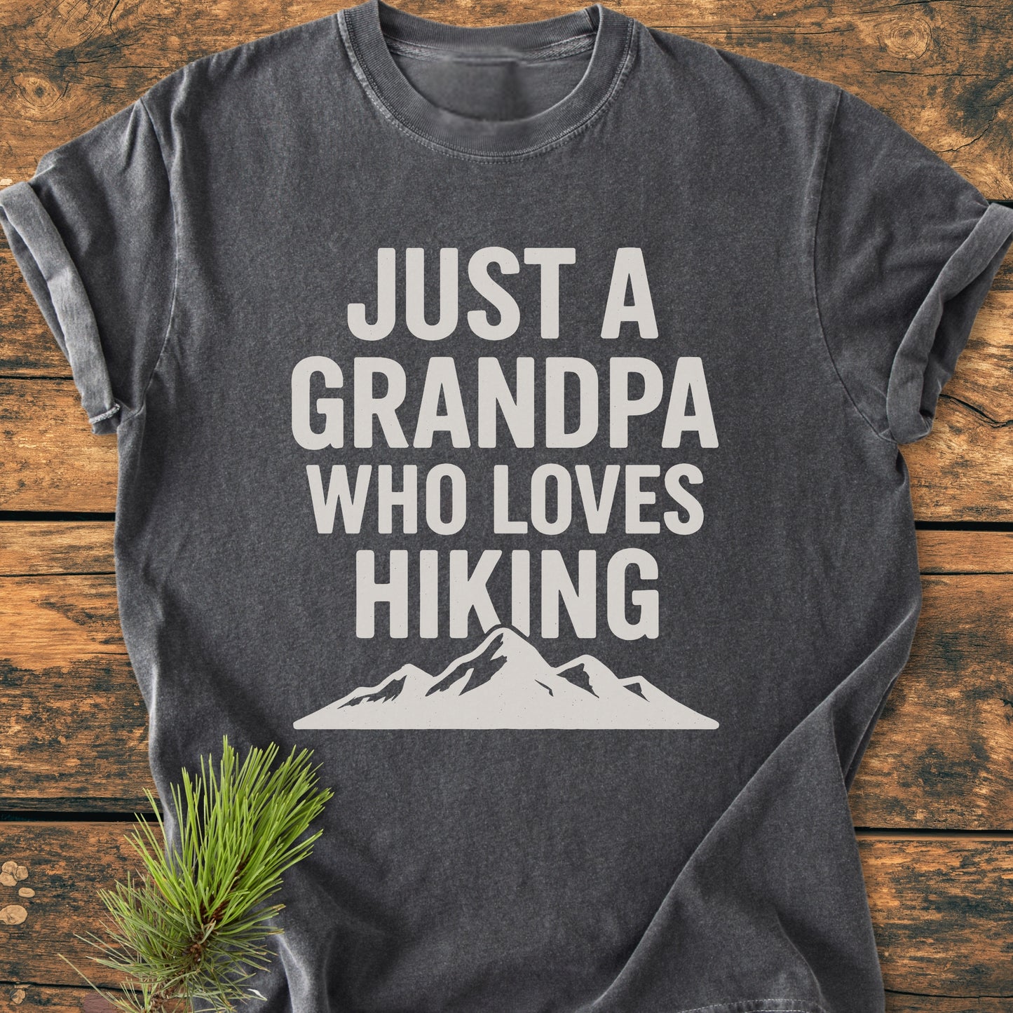 Hiking Grandpa - Vintage Wash Tee featuring bold white text and mountain silhouette on a dark-charcoal gray background, styled with a pine branch, highlighting its relaxed fit and durable design.