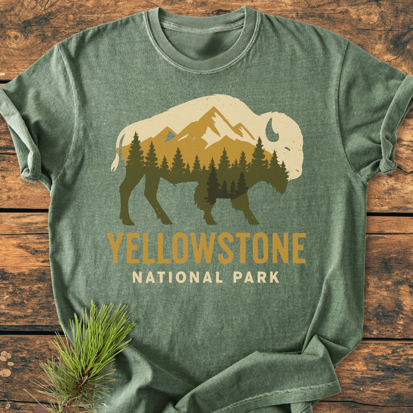 Yellowstone Bison - Vintage Wash Tee featuring a bison silhouette with mountain and tree design, displayed on a wooden surface with a pine sprig nearby, highlights its relaxed fit and durability.