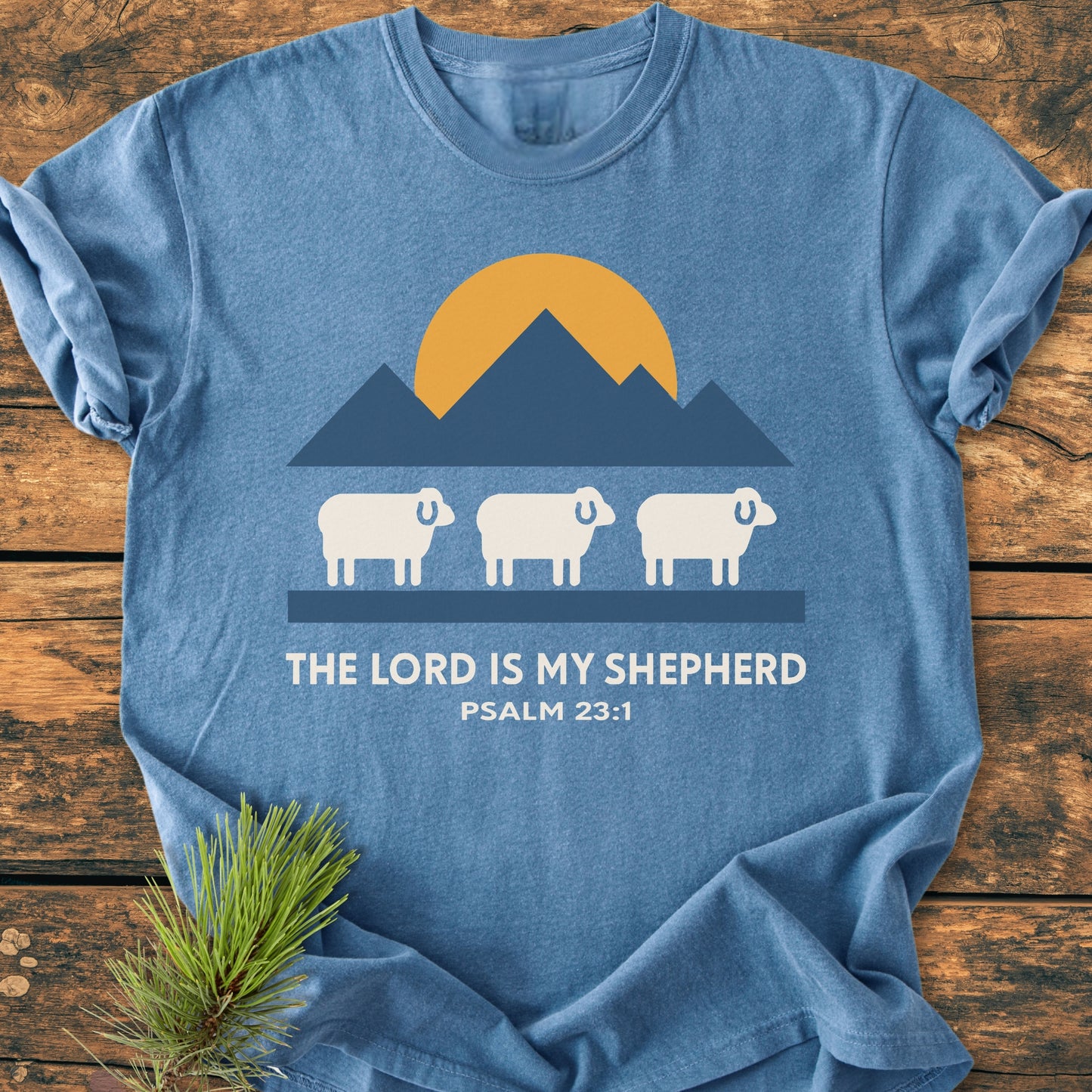The Lord Is My Shepherd - Vintage Wash Tee features a graphic of sheep, mountains, and a rising sun, with THE LORD IS MY SHEPHERD text. It's a relaxed fit, garment-dyed, cotton shirt.