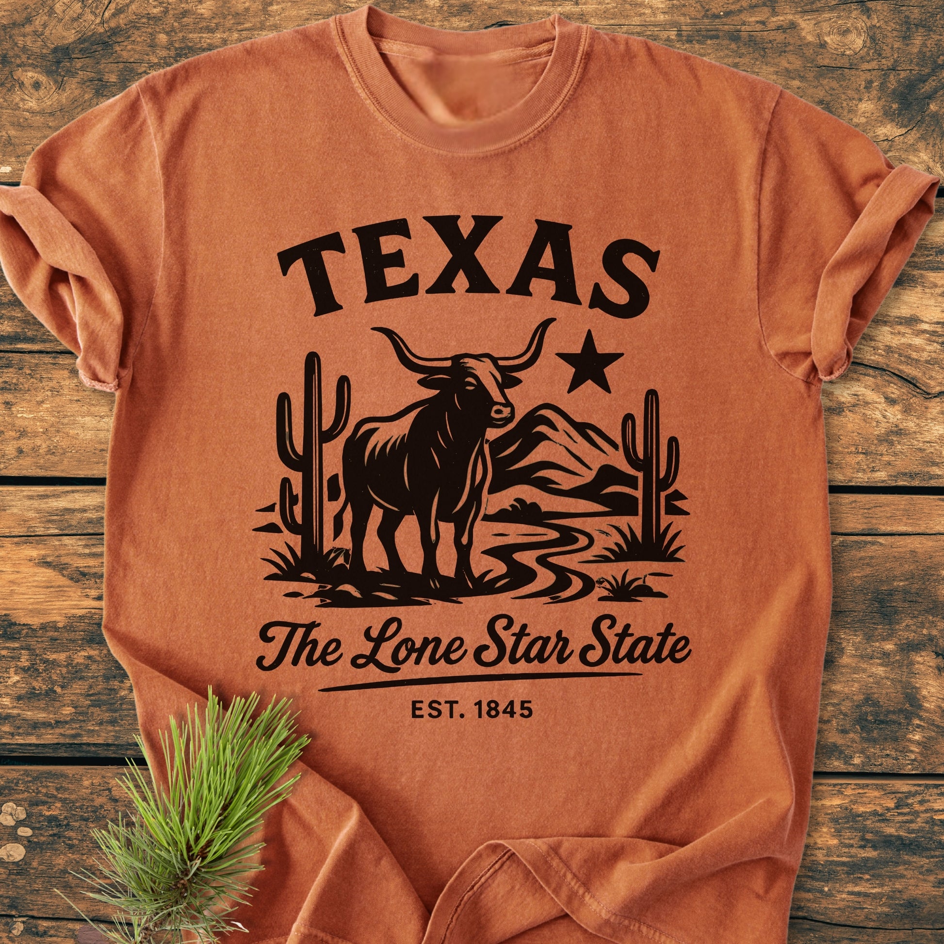 Texas, The Lone Star State - Vintage Wash Tee features a western graphic with a longhorn steer and desert scene. Made from soft, pre-shrunk cotton, it's laid flat beside a pine sprig.