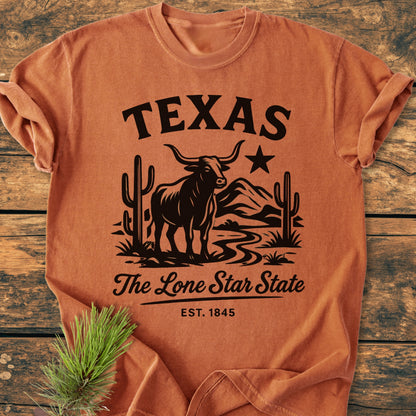 Texas, The Lone Star State - Vintage Wash Tee features a western graphic with a longhorn steer and desert scene. Made from soft, pre-shrunk cotton, it's laid flat beside a pine sprig.