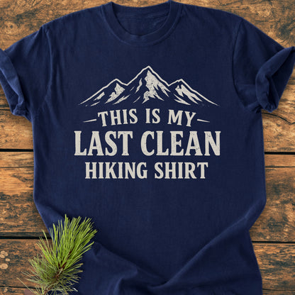 Navy-blue Last Clean Hiking Shirt - Vintage Wash Tee with a stylized mountain graphic and slogan, laid on wood with pine sprigs, showcasing its relaxed fit and durable, soft-washed fabric.