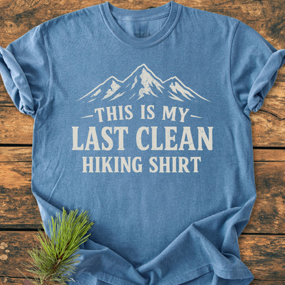 Heather-blue Last Clean Hiking Shirt - Vintage Wash Tee with white mountain graphic and bold text, laid flat on wood. Pine sprig accentuates the tee's rustic, outdoor theme.