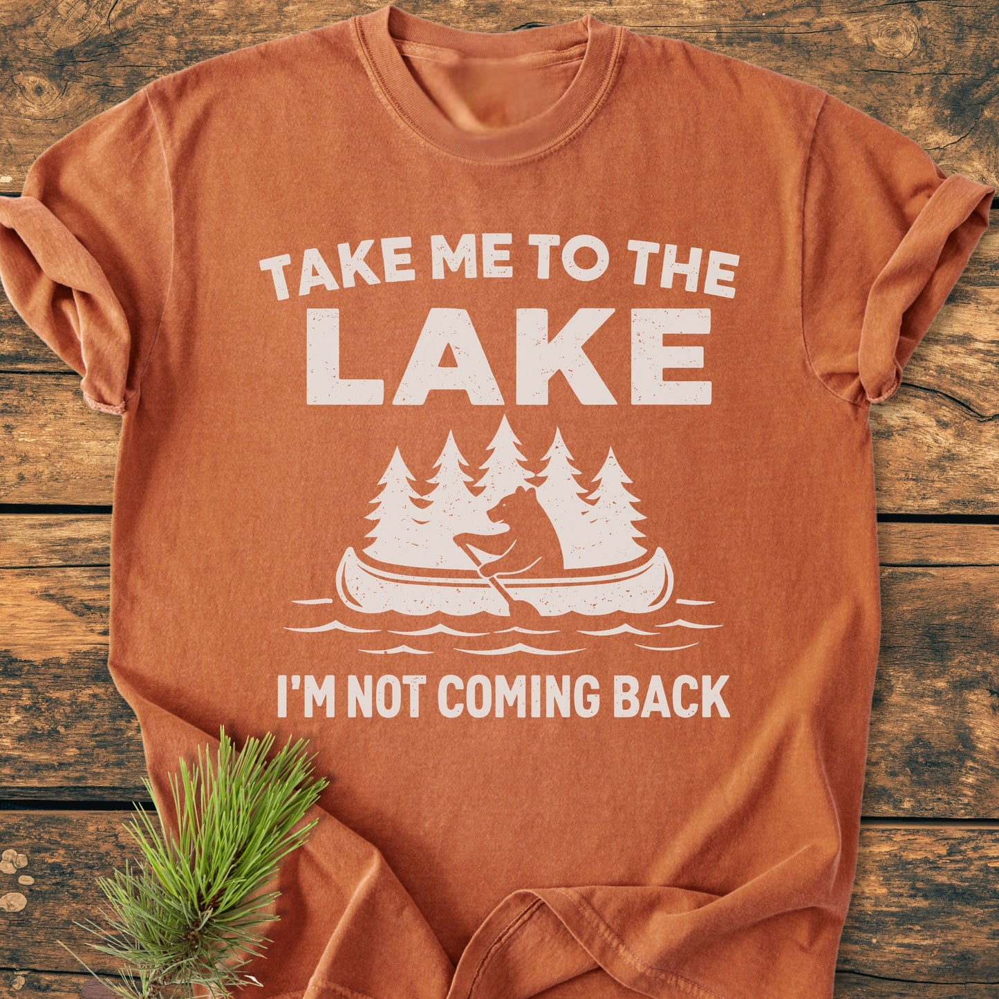 Take Me To The Lake - Vintage Wash Tee featuring a bear in a canoe graphic on soft, garment-dyed fabric, laid flat with a pine sprig accentuating its relaxed, comfortable style.