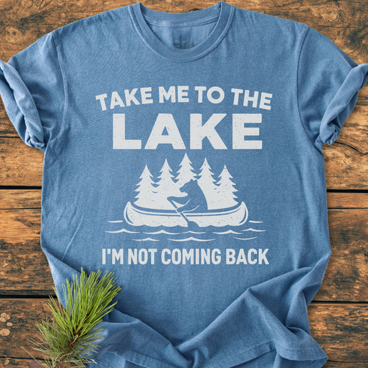 Take Me To The Lake - Vintage Wash Tee features a bear paddling a canoe graphic with pine trees, on a heather-blue T-shirt, laid on wood; emphasizes comfort and durability with garment-dyed cotton.