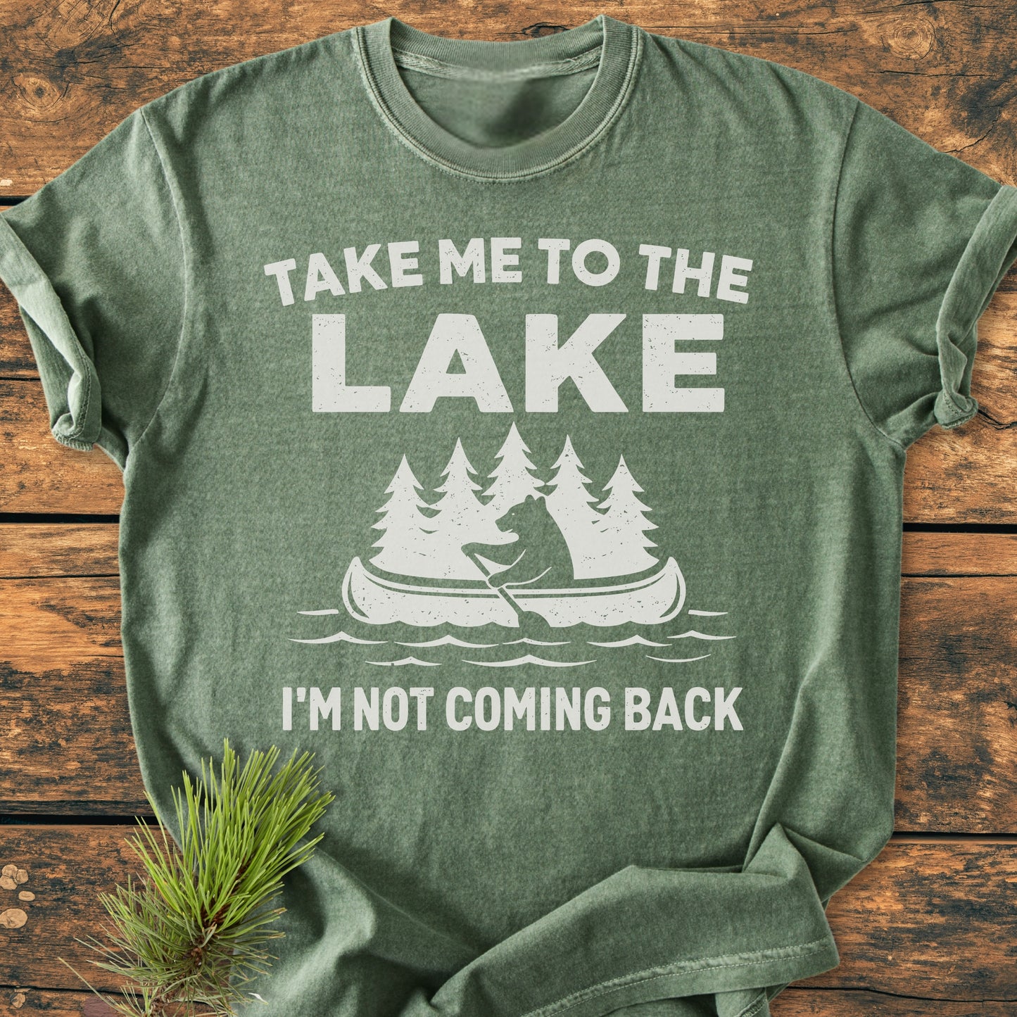 Take Me To The Lake - Vintage Wash Tee features a white print with a canoe and pine trees on soft, heather-green fabric. Made from 100% ring-spun cotton, it offers a relaxed fit.