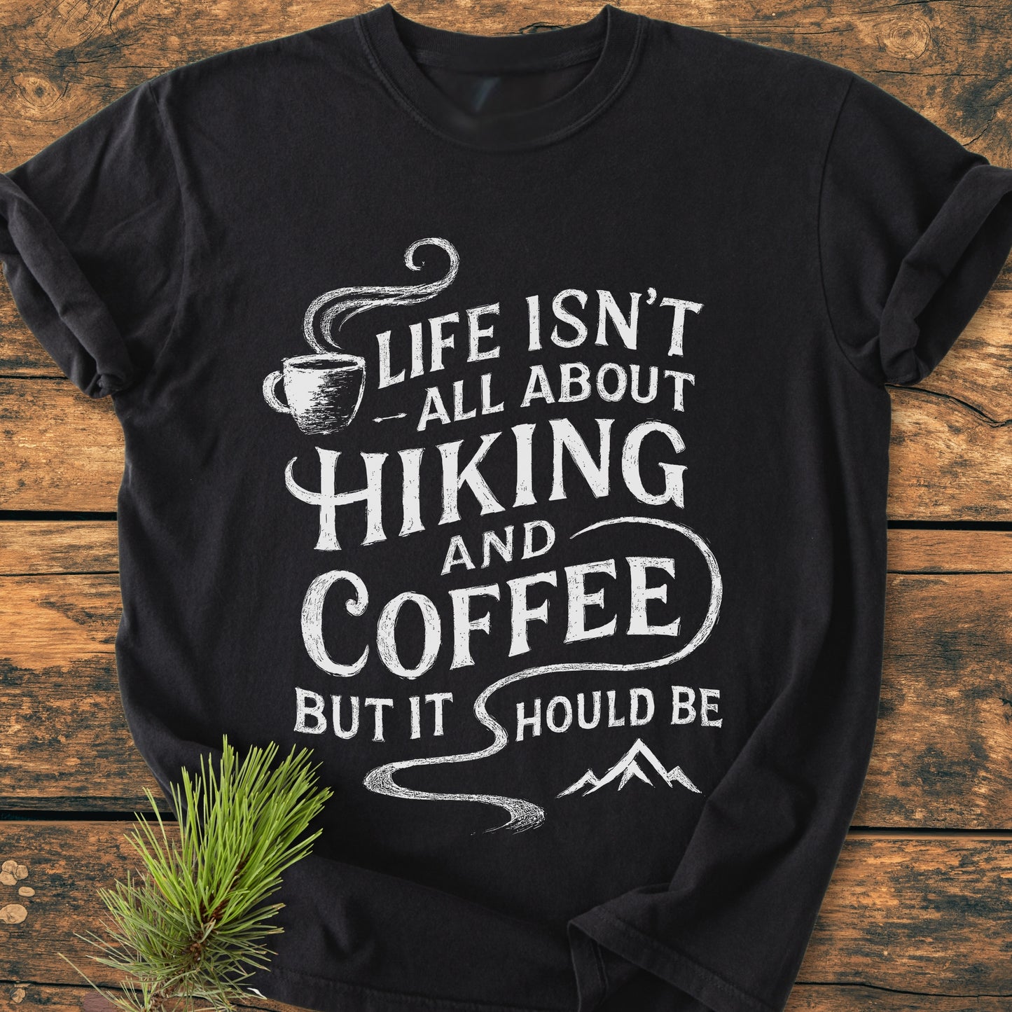 Hiking And Coffee - Vintage Wash Tee with a white slogan and icons, laid flat on wood. Made from soft, durable, 100% ring-spun cotton for a cozy, relaxed fit.