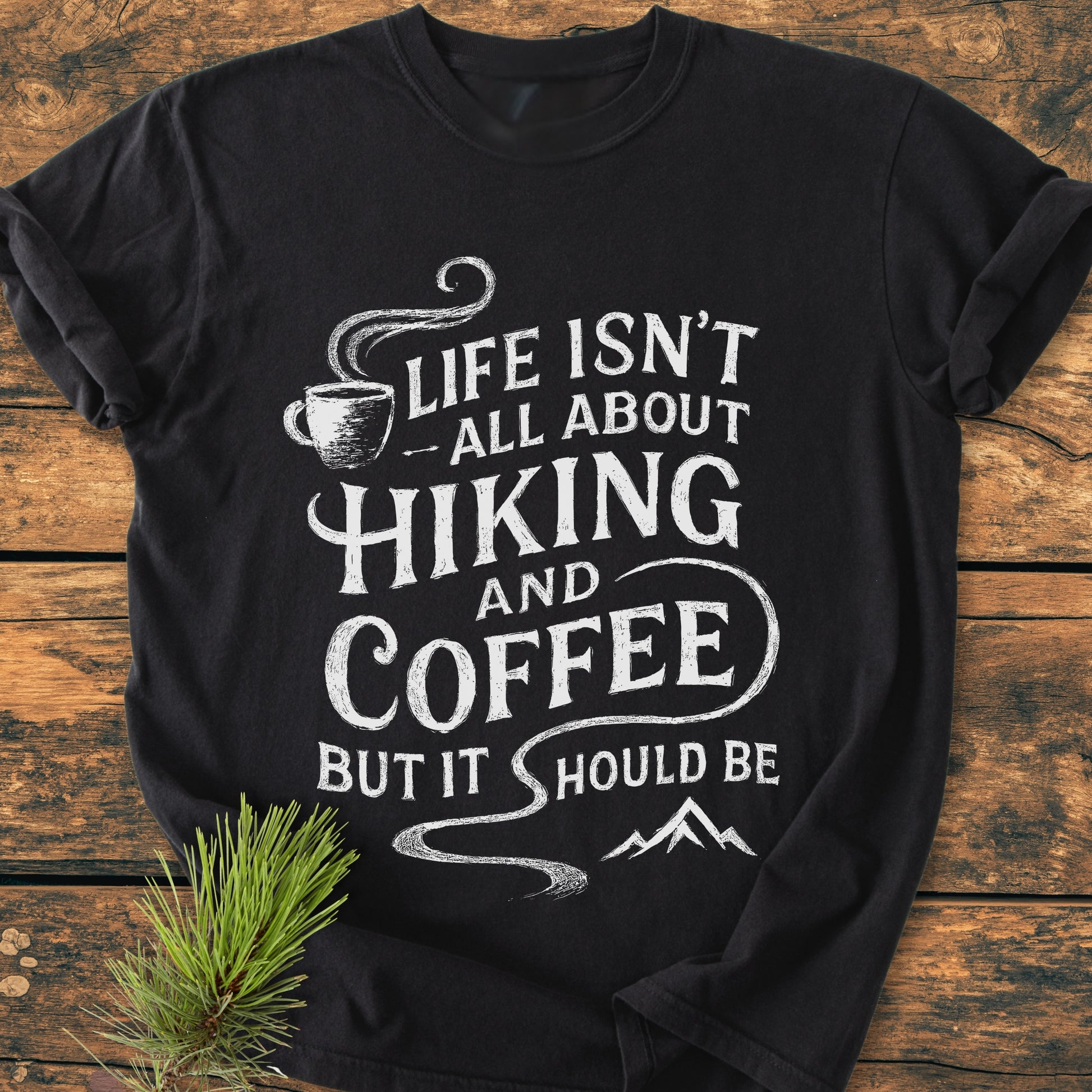 Hiking And Coffee - Vintage Wash Tee with a white slogan and icons, laid flat on wood. Made from soft, durable, 100% ring-spun cotton for a cozy, relaxed fit.