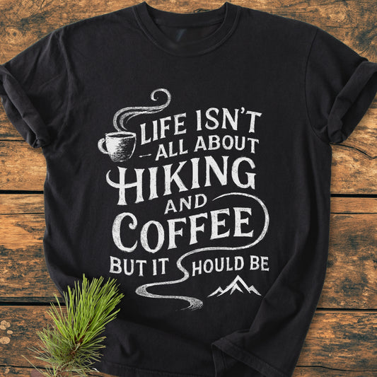 Hiking And Coffee - Vintage Wash Tee with a white slogan and icons, laid flat on wood. Made from soft, durable, 100% ring-spun cotton for a cozy, relaxed fit.