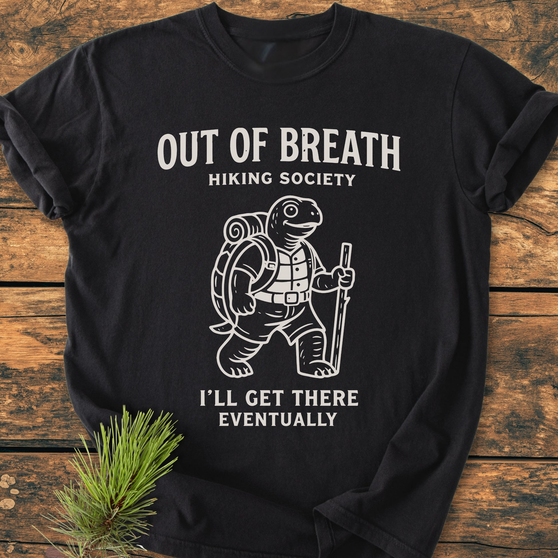 Out Of Breath Turtle - Vintage Wash Tee features a hiking turtle with a sleeping mat and stick, humorously captioned, designed on a soft, durable black T-shirt, enhanced by a pine sprig accent.