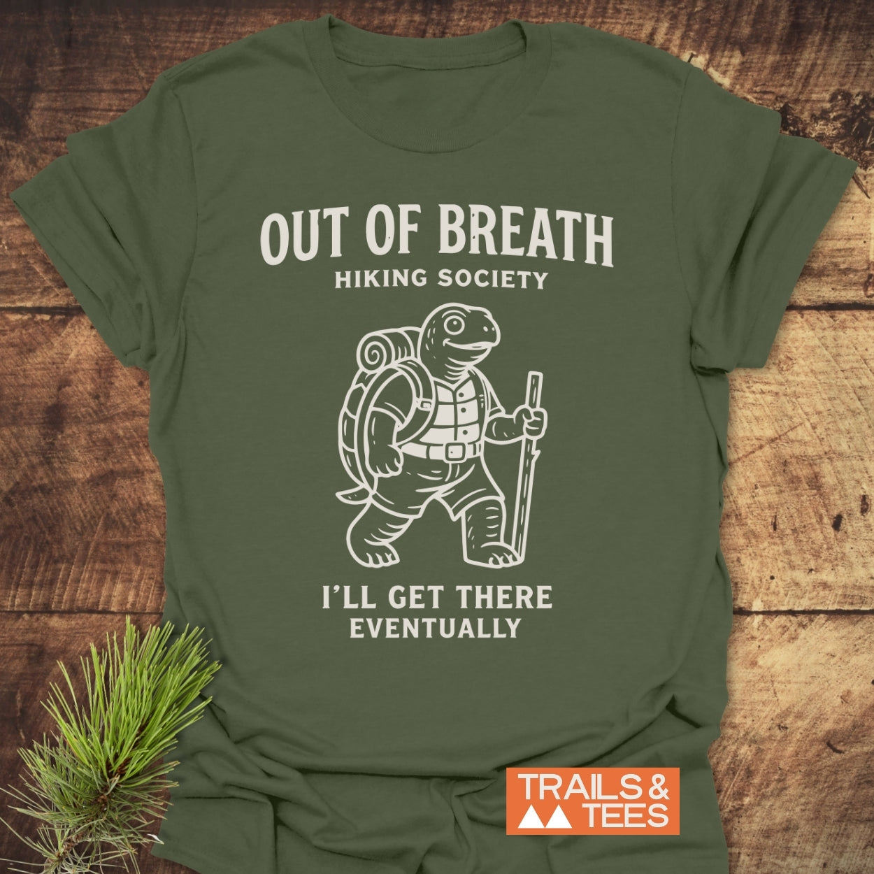 Out Of Breath Turtle T-Shirt featuring a hiking turtle cartoon with text Hiking Society and I'll Get There Eventually, small Trails & Tees logo on an olive-green background.