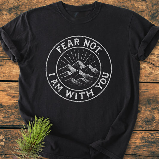 Fear Not - Vintage Wash Tee featuring a white chalk-style emblem of mountains and sun rays, laid on wood with a pine sprig beside, highlighting its rustic charm and cozy, relaxed fit.