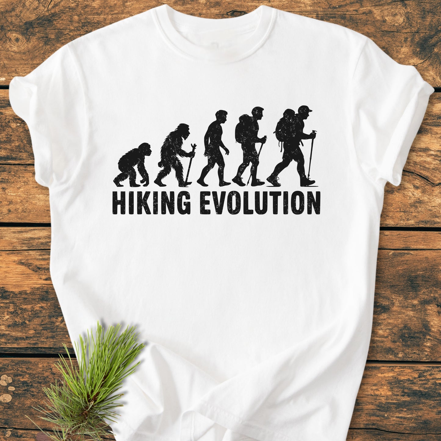 Hiking Evolution - Vintage Wash Tee: White T-shirt on wood, featuring black evolution graphic of hikers and HIKING EVOLUTION text. Cozy, relaxed fit; made from soft-washed, pre-shrunk 100% ring-spun cotton.