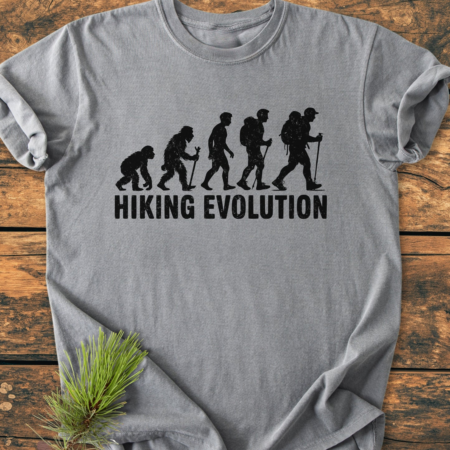 Hiking Evolution - Vintage Wash Tee featuring an evolution-themed graphic with hikers, printed on soft, light-gray fabric, showcasing its relaxed fit and durability. A pine twig accents the shirt's design.