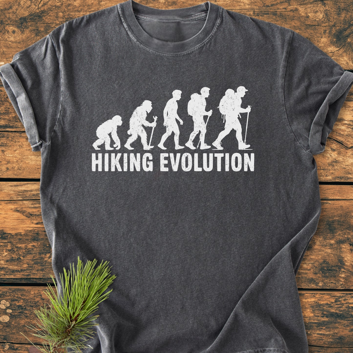 Hiking Evolution - Vintage Wash Tee with evolution graphic from primate to backpacker on charcoal fabric. Laid flat on wood, this comfortable, ring-spun cotton T-shirt embodies outdoor adventure.