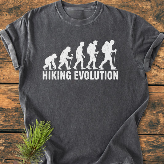 Hiking Evolution - Vintage Wash Tee with evolution graphic from primate to backpacker on charcoal fabric. Laid flat on wood, this comfortable, ring-spun cotton T-shirt embodies outdoor adventure.
