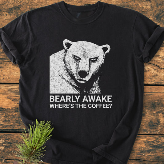 Bearly Awake - Vintage Wash Tee: Black T-shirt featuring a distressed bear's head graphic and humorous caption, laid on wood with a pine sprig. Made from soft, durable, pre-shrunk 100% ring-spun cotton.