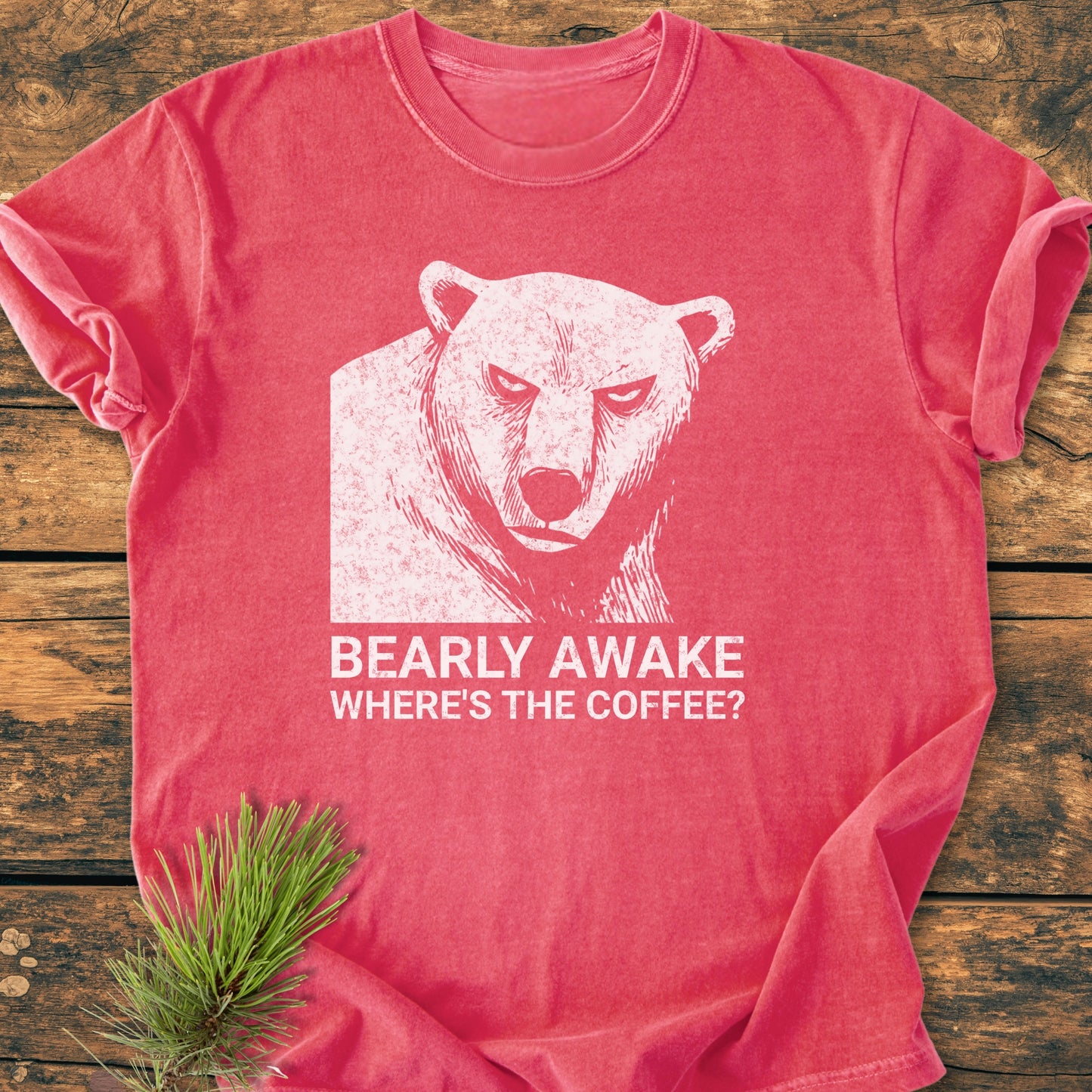 Bearly Awake - Vintage Wash Tee on rustic wood, features a grumpy bear print with slogan. Soft-washed, rose hue, pine needle accent, highlighting cozy, relaxed fit and durable craftsmanship.