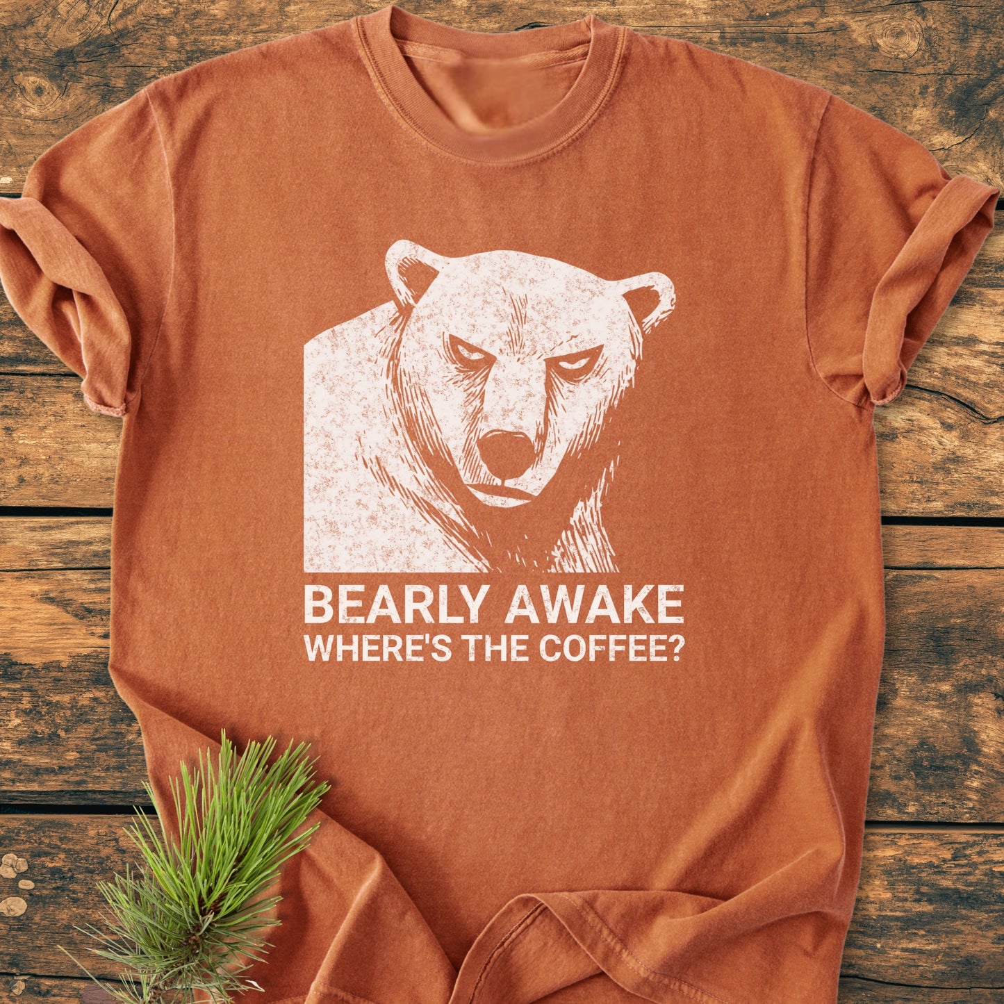 Bearly Awake - Vintage Wash Tee features a distressed white bear graphic with BEARLY AWAKE WHERE’S THE COFFEE? slogan on rust-orange fabric, laid on wood, with visible soft, relaxed fit.