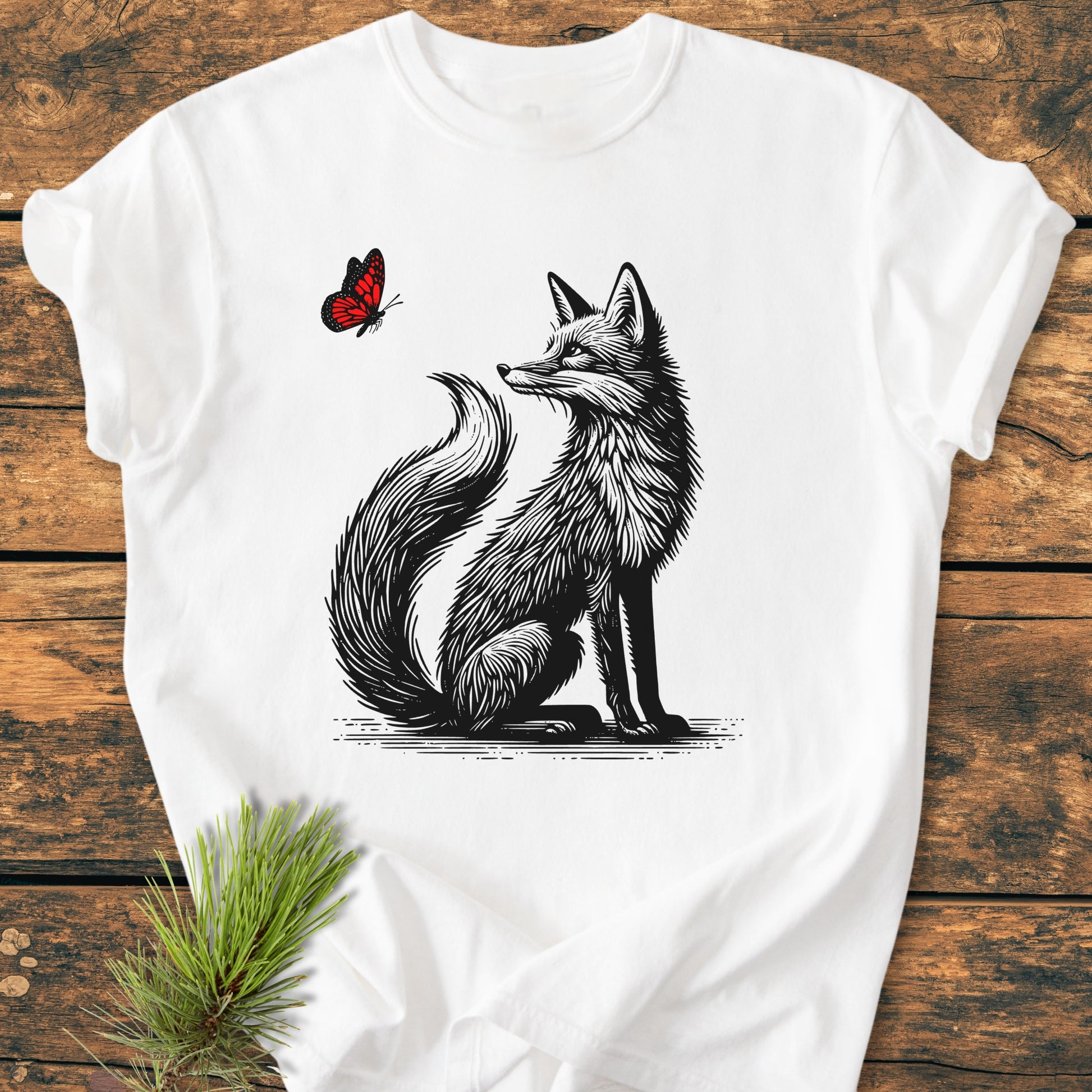 Fox And Butterfly - Vintage Wash Tee featuring a black line-art fox gazing at a red butterfly, laid flat on a wooden surface. Made of soft, pre-shrunk 100% ring-spun cotton for comfort.